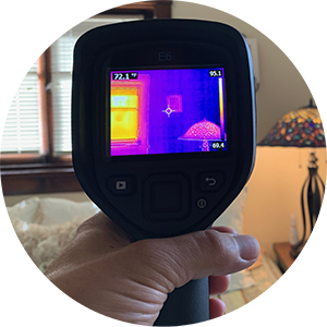 Hand holding a thermal imaging camera measuring heat-loss in a living room.