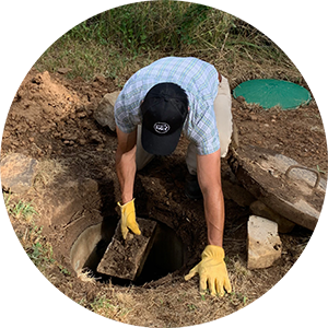 Person with yellow gloves and work boots opening up the cover of a septic tank.